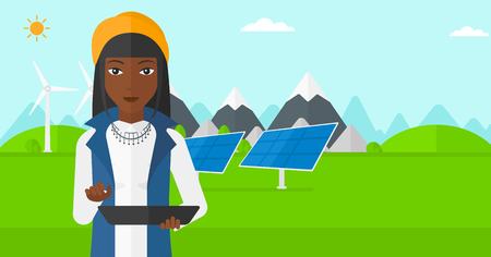 An african-american woman holding a tablet computer in hands on a background with solar pannels and wind turbins vector flat design illustration. Horizontal layout.のイラスト素材