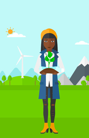 An african-american woman standing on a background with wind turbins and holding in hands a plastic bottle with a small plant growing inside vector flat design illustration. Vertical layout.のイラスト素材