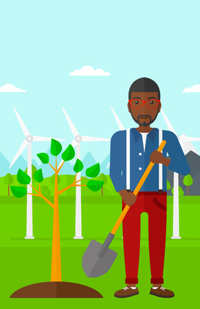 An african-american man with the shovel plants a tree on a background with wind turbins vector flat design illustration. Vertical layout.のイラスト素材