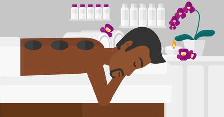 An african-american man relaxing while getting stone therapy massage on the background of spa center vector flat design illustration. Horizontal layout.のイラスト素材
