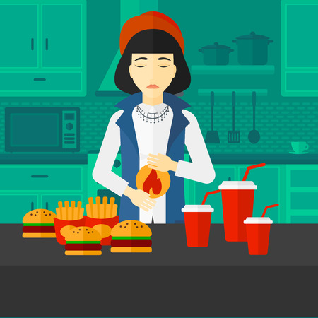An asian woman standing in the kitchen in front of table full of junk food and suffering from heartburn vector flat design illustration. Square layout.のイラスト素材