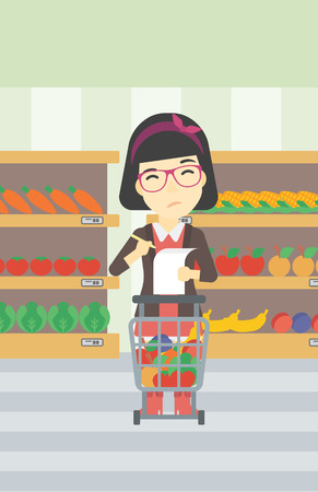 An asian thoughtful woman standing at the supermarket with supermarket trolley full with products and holding a shopping list in hands. Vector flat design illustration. Vertical layout.のイラスト素材