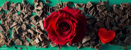 Red rosebud with chopped chocolate for St Valentine's day on a green wooden backdrop, top viewの写真素材