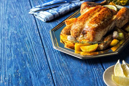 Lemon and thyme roasted chicken with roasted crispy potatoes on a blue wooden background with...
