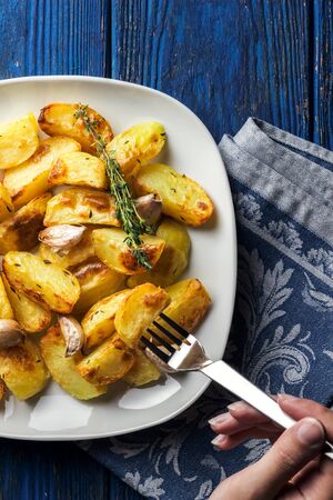 Crispy roasted potatoes with garlic and thyme on a blue wooden background with a vintage napkin, flat layの写真素材