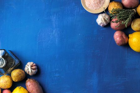 Starchy yellow and red potatoes with fresh thyme, garlic and lemon on a blue wooden background, flat layの写真素材