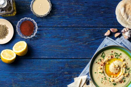 Chickpea hummus and various middle-eastern vegetarian ingredients on a dark blue wooden background