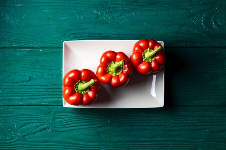 Red bell pepper on a white plate on a dark green wooden background