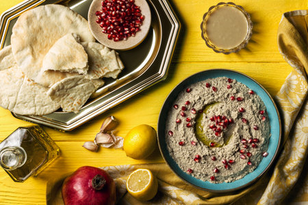Baba ganoush or mutabal, Middle Eastern eggplant dip sauce garnished with pomegranate seeds, with various ingredients and served in a light blue plate on a yellow wooden table with a rustic napkinの写真素材