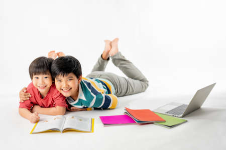 Portrait of Happy asian boys, Brother on floor with laptop and books isolated on white background,...