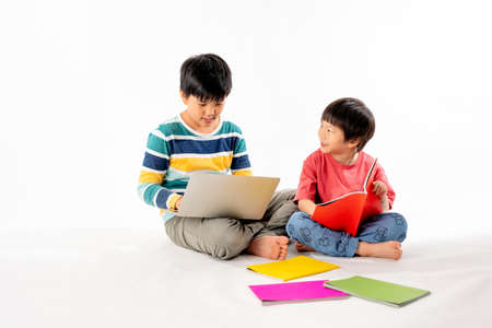 Portrait of Happy asian boys, Brother on floor with laptop and books isolated on white background, Education and learning with technology conceptの写真素材