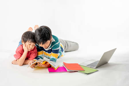 Portrait of Happy asian boys, Brother on floor with laptop and books isolated on white background, Education and learning with technology conceptの写真素材