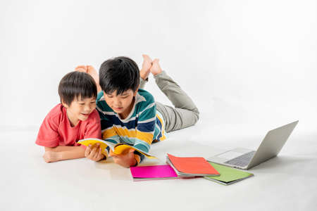 Portrait of Happy asian boys, Brother on floor with laptop and books isolated on white background, Education and learning with technology conceptの写真素材