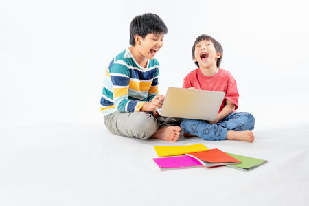 Portrait of Happy asian boys, Brother on floor with laptop and books isolated on white background, Education and learning with technology conceptの写真素材