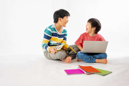 Portrait of Happy asian boys, Brother on floor with laptop and books isolated on white background, Education and learning with technology conceptの写真素材