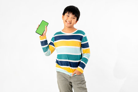Young Asian Kid holding a phone in his hands with a green screen standing on a white isolated background with copy space.の写真素材