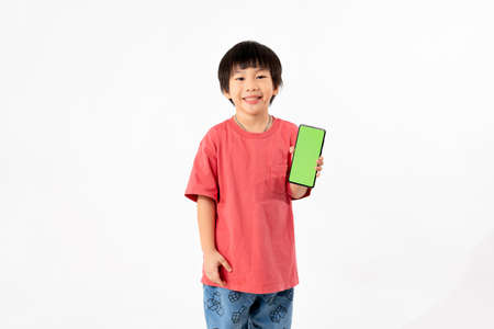 Young Asian Kid holding a phone in his hands with a green screen standing on a white isolated background with copy space.の写真素材