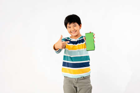 Young Asian Kid holding a phone in his hands with a green screen standing on a white isolated background with copy space.の写真素材