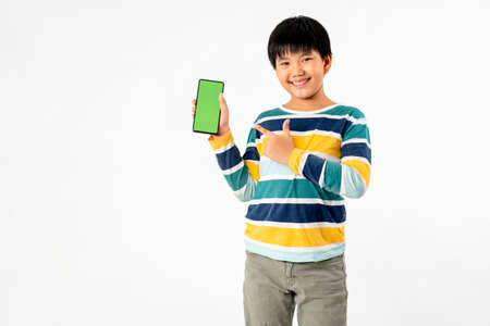 Young Asian Kid holding a phone in his hands with a green screen standing on a white isolated background with copy space.の写真素材