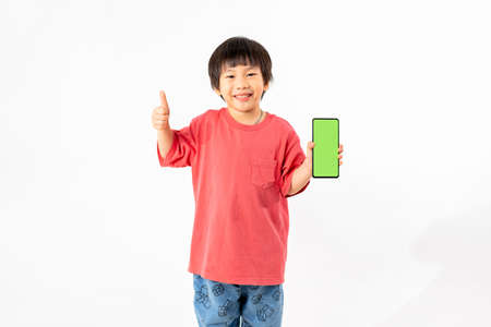 Young Asian Kid holding a phone in his hands with a green screen standing on a white isolated background with copy space.の写真素材