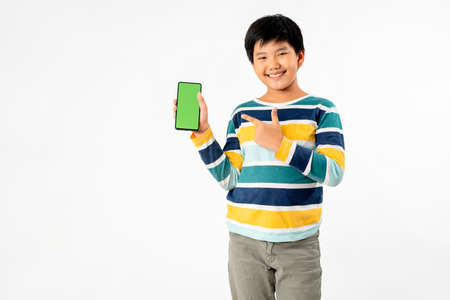 Young Asian Kid holding a phone in his hands with a green screen standing on a white isolated background with copy space.の写真素材