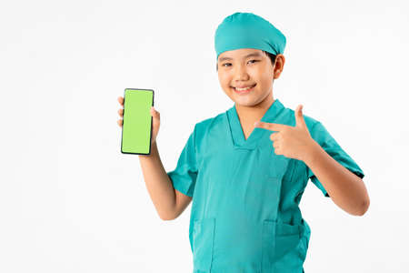 Portrait of Young Asian Boy Dressing to be Doctor, Holding Smart phone with Green Screen Isolate on White Background, Education and Technology Conceptの写真素材