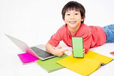 Portrait of Happy asian boy holding a phone in his hands with a green screen on floor with with laptop and books isolated on white background with copy space, Education and learning with technology conceptの写真素材