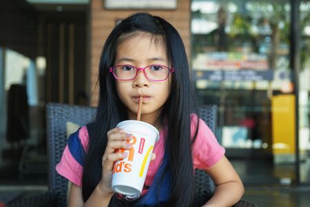 BANGKOK ,THAILAND - JANUARY 19, 2019 : little Asian girl drank cold drink from straw in front of  McDonald's restaurant and cafeのeditorial素材