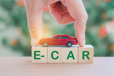 human's hand holding red miniature vehicle above wooden cubes with e-car word, on blurred nature background means electric car for campaign of save world, alternative conceptの写真素材