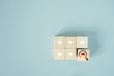 red arrow inside of magnifier glass icon on wooden cube blocks and different direction from other white arrows for focus business disruption and technology transformation conceptの写真素材
