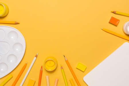 Artist workplace with watercolor, gouache, acrylic, palette, pencils, pastel, sketchbook on yellow background. Flat lay. Top view. Artistic wallpaperの写真素材
