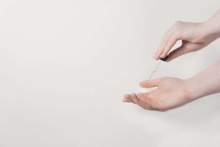 Woman with pastel manicure used serum dropping on her hand on white textured background. Skin care...