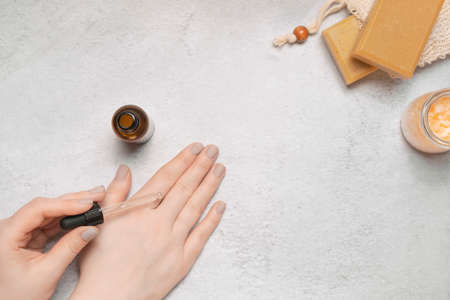 Woman with pastel manicure used serum dropping on her hand. Zero waste organic cosmetics on light...
