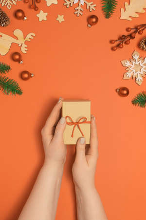 Womans hands with pastel manicure holding craft gift or present box on orange pastel table with christmas decoration. Flat lay top viewの写真素材