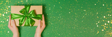 Banner with woman holding craft present box with ribbon as presenf for Christmas, fathers day, birthday on green background. Flat lay, copy spaceの写真素材