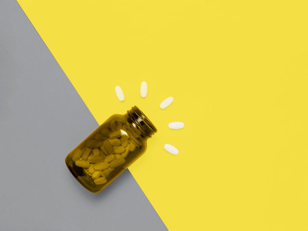 Medical pills spilling out of glass bottle on Illuminating Yellow and Ultimate Gray background. Creative design demonstrating colors of the year 2021の写真素材