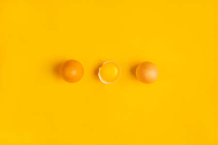 Three farm brown chicken eggs with one yolk on yellow table. Minimalistic product concept. Healthy...
