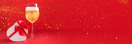 Banner with glass of champagne, heart shaped gift box and lights on red background. Romantic present for Valentines Day, womens day, mothers dayの写真素材