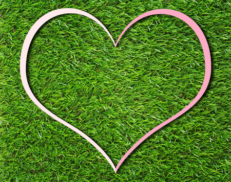 Creative pink heart paper frame on green grass background, love and nature conceptの写真素材