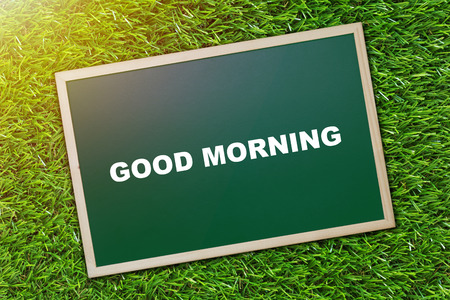Good morning and wake up concept, greeting text on blackboard, green grass backgroundの写真素材
