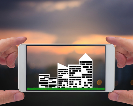 Smart city concept, group of building and green grass on blur background, mobile phone, ecology and nature friendlyの写真素材