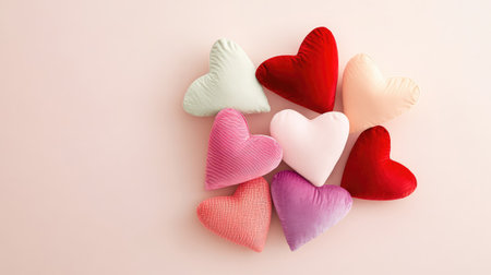 An aesthetically pleasing arrangement of colorful heart-shaped cushions in various shades on a soft pink background, perfect for romantic and festive decor.の素材