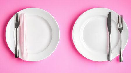 Two elegant white plates adorned with silver cutlery and a soft pink napkin create a stunning contrast against a vibrant pink background, ideal for dining aesthetics.の素材