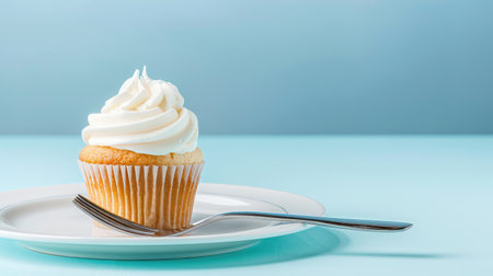 A stunning cupcake with creamy frosting sits on a white plate, accompanied by a silver fork. The soft blue background enhances the fresh and inviting aesthetic of this delightful dessert.の素材