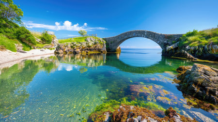 Discover a tranquil coastal scene featuring a historic arch bridge over crystal-clear waters. Lush greenery and bright blue skies enhance the serene landscape.の素材
