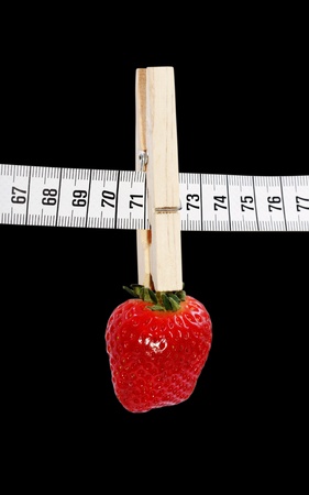 One strawberry hanging on the measuring tape with clothespin isolated on a black surface.の写真素材