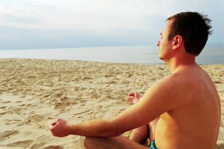 Young man is meditation on the beach at the sea.の写真素材