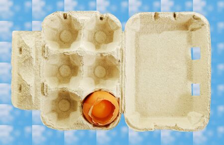 One broken egg in a box, isolated on blue surface.の写真素材