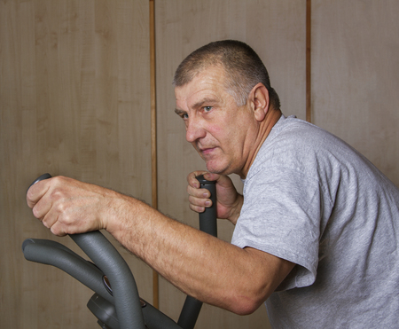 Muscular adult man is training by exercise bike.の写真素材