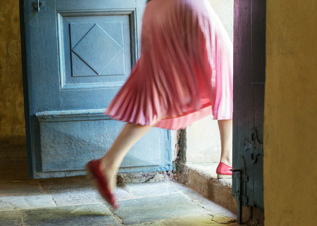 Woman in pink steps over the threshold of an old house.の写真素材